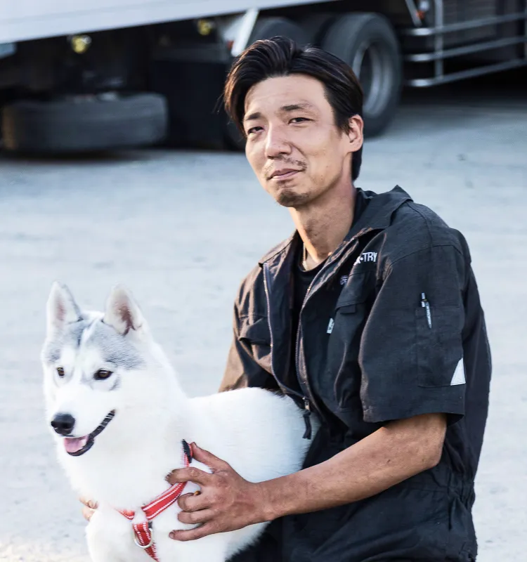 白いハスキー犬と一緒に座る整備士風の男性。