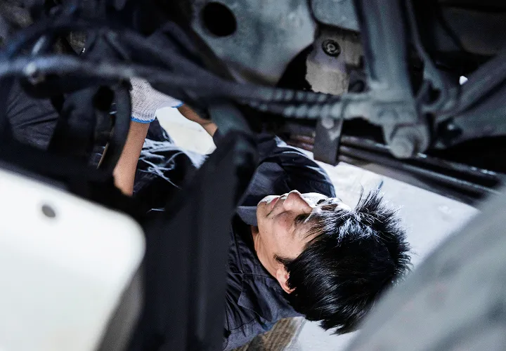 整備士が車のエンジンルーム下から部品を確認している様子。
