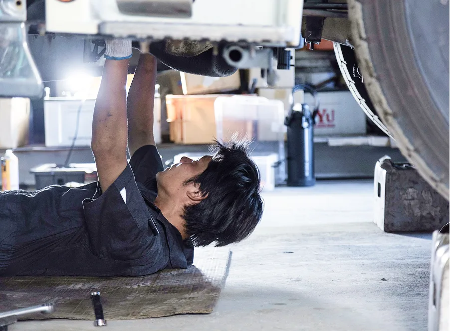 仰向けで車両の下から整備作業を行う整備士。